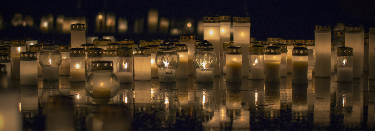 Viele brennende Friedhofskerzen in der Nacht bei Regen