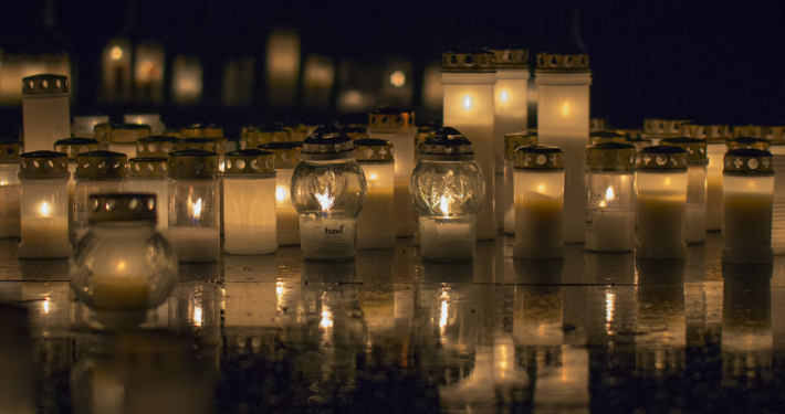 Viele brennende Friedhofskerzen in der Nacht bei Regen