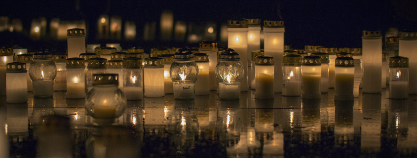 Viele brennende Friedhofskerzen in der Nacht bei Regen