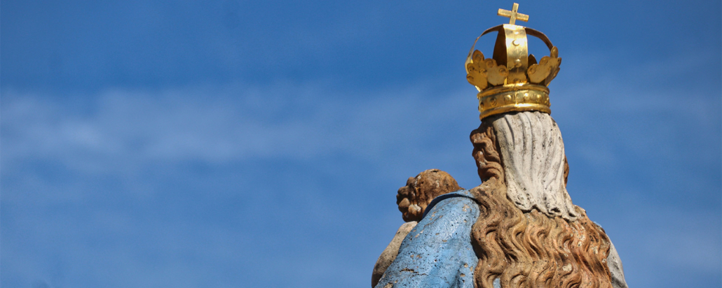 Eine Marienstatue von hinten vor blauem Himmel