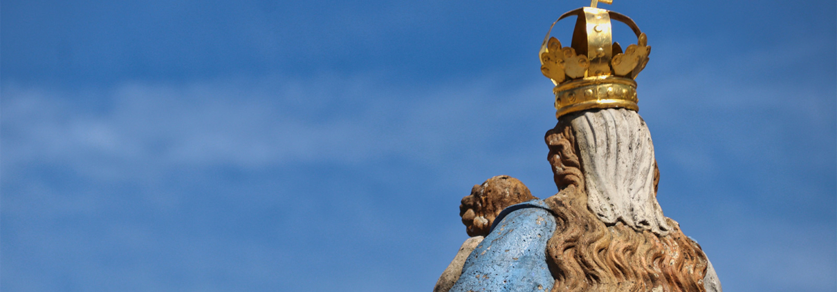 Eine Marienstatue von hinten vor blauem Himmel