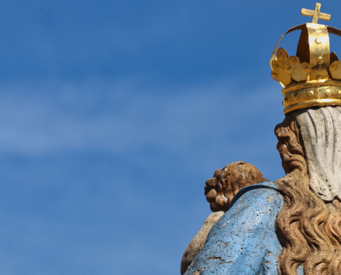 Eine Marienstatue von hinten vor blauem Himmel