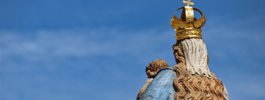 Eine Marienstatue von hinten vor blauem Himmel