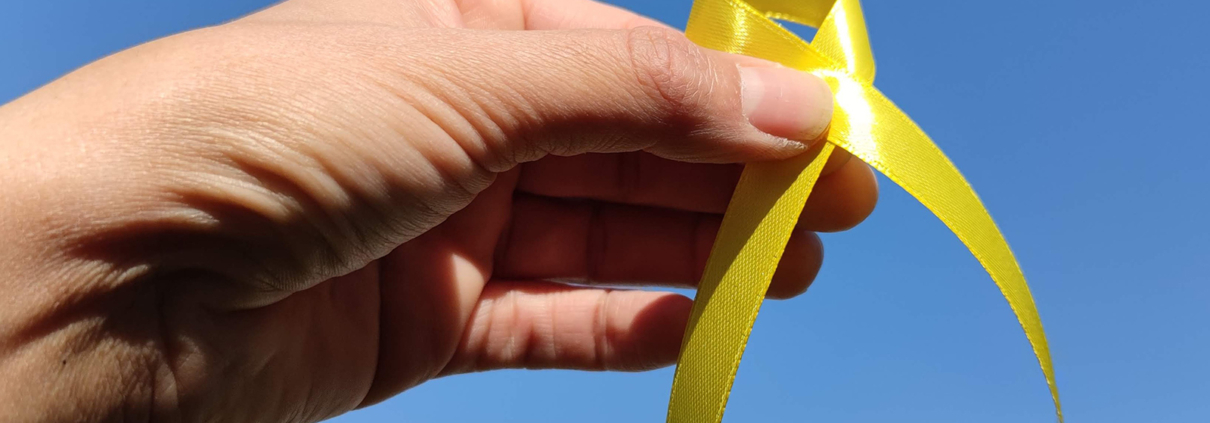 Hand mit gelbem Band vor blauem Himmel