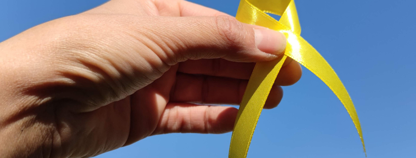 Hand mit gelbem Band vor blauem Himmel