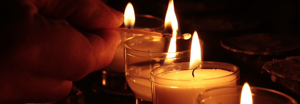 Eine Hand zündet Opferlichter in einer Kirche an