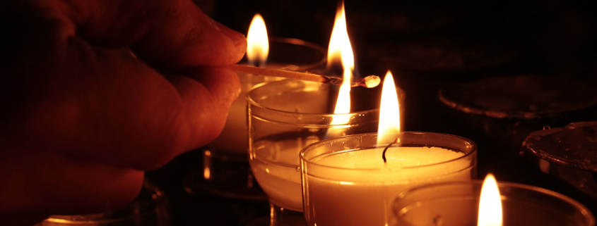 Eine Hand zündet Opferlichter in einer Kirche an