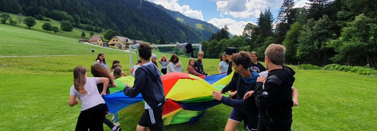 Kinder spielen mit einem großen Tuch auf einer Wiese