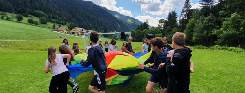 Kinder spielen mit einem großen Tuch auf einer Wiese