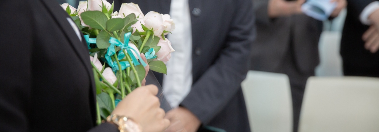 Eine Begräbnisszene mit Menschen ud weißen Rosen