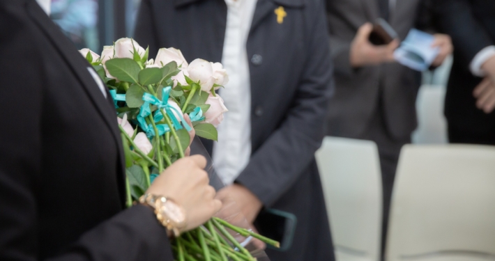 Eine Begräbnisszene mit Menschen ud weißen Rosen