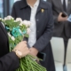 Eine Begräbnisszene mit Menschen ud weißen Rosen
