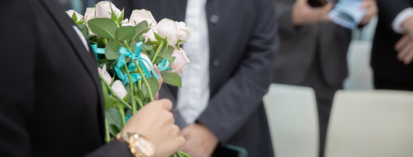 Eine Begräbnisszene mit Menschen ud weißen Rosen