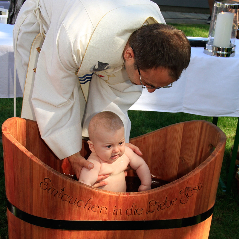 Pfarrer Martin tauft ein Baby in einem Bottich