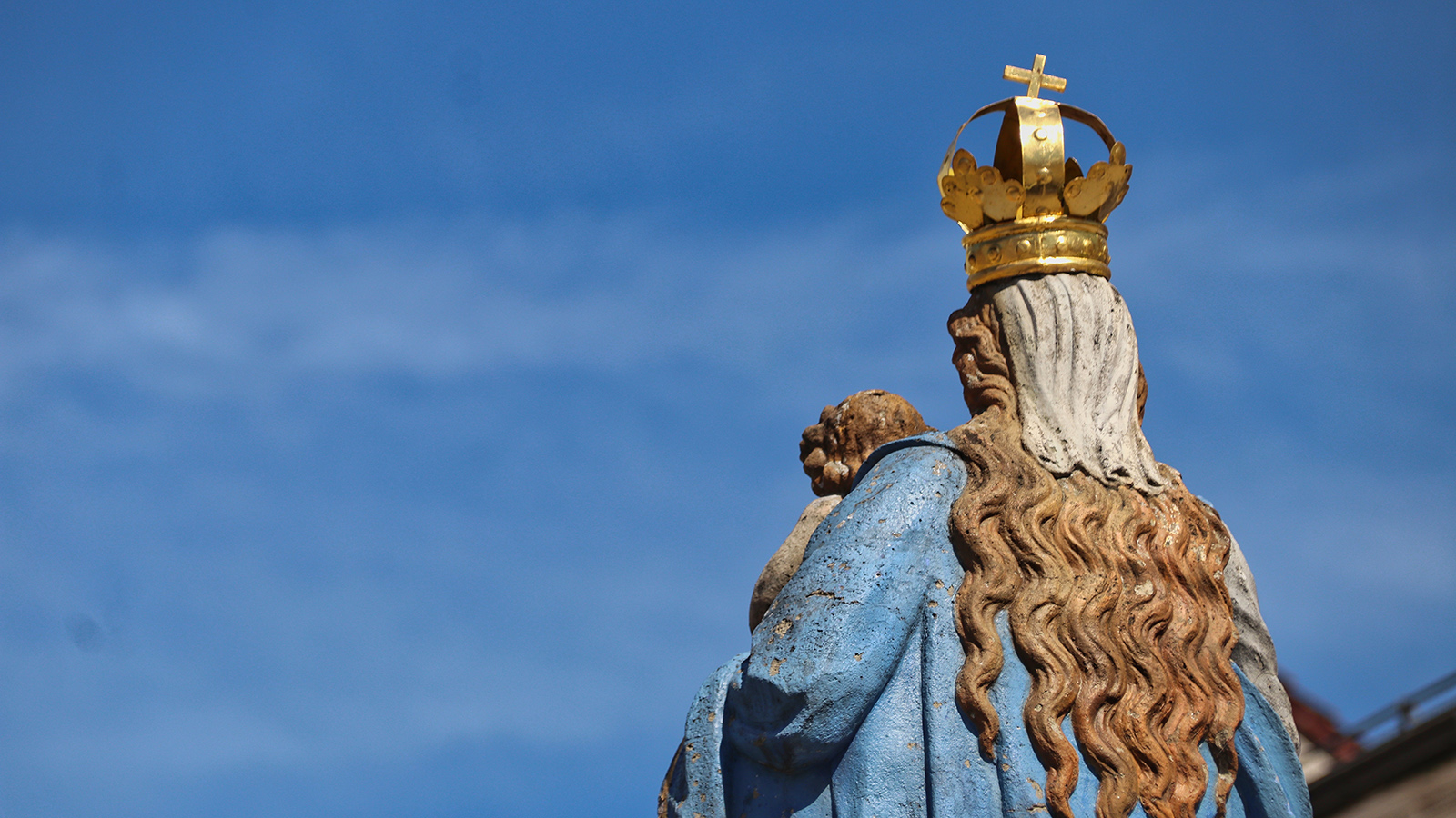 Eine Marienstatue von hinten vor blauem Himmel