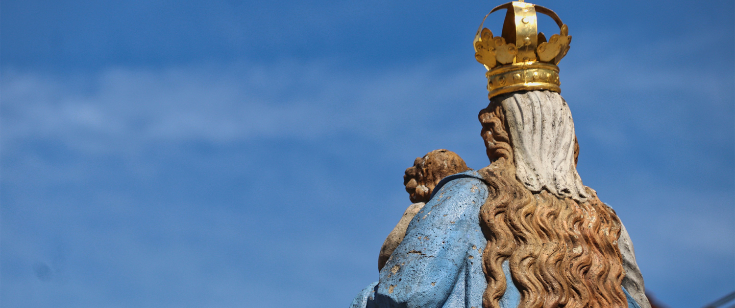 Eine Marienstatue von hinten vor blauem Himmel