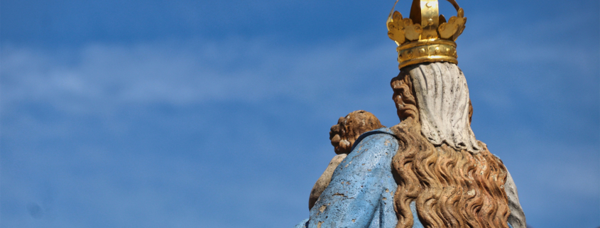 Eine Marienstatue von hinten vor blauem Himmel