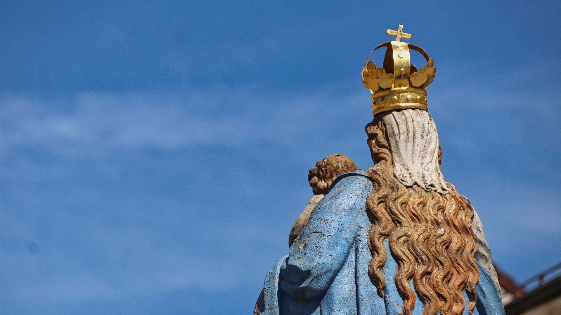 Eine Marienstatue von hinten vor blauem Himmel