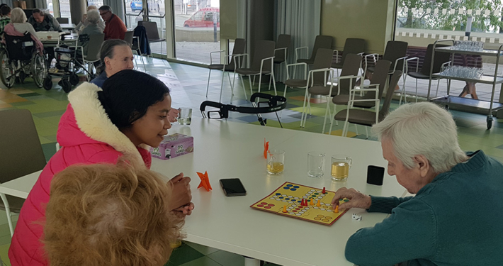 Ein Mädchen spielt Mensch-ärgere Dich-nicht mit Senioren