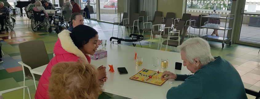 Ein Mädchen spielt Mensch-ärgere Dich-nicht mit Senioren
