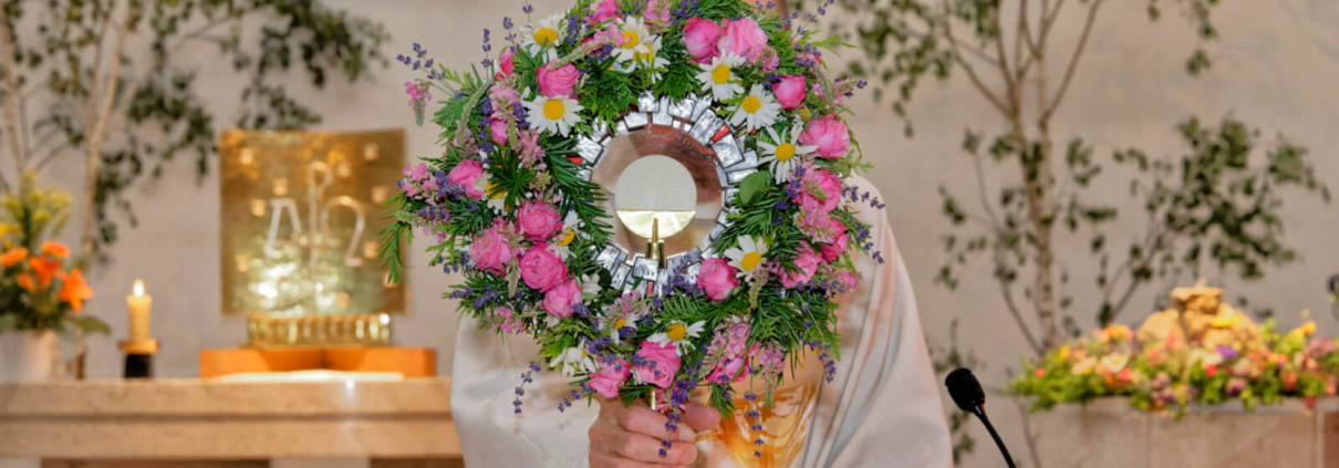 Ein Priester hält eine blumengeschmückte Monstranz in der Kirche Schönbrunn-Vorpark