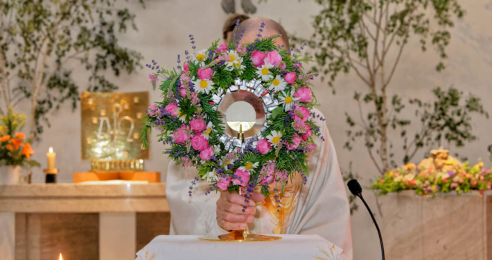 Ein Priester hält eine blumengeschmückte Monstranz in der Kirche Schönbrunn-Vorpark