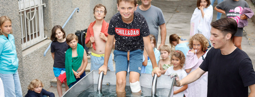 Ein Kind steigt in ein großes Taufbecken aus Metall