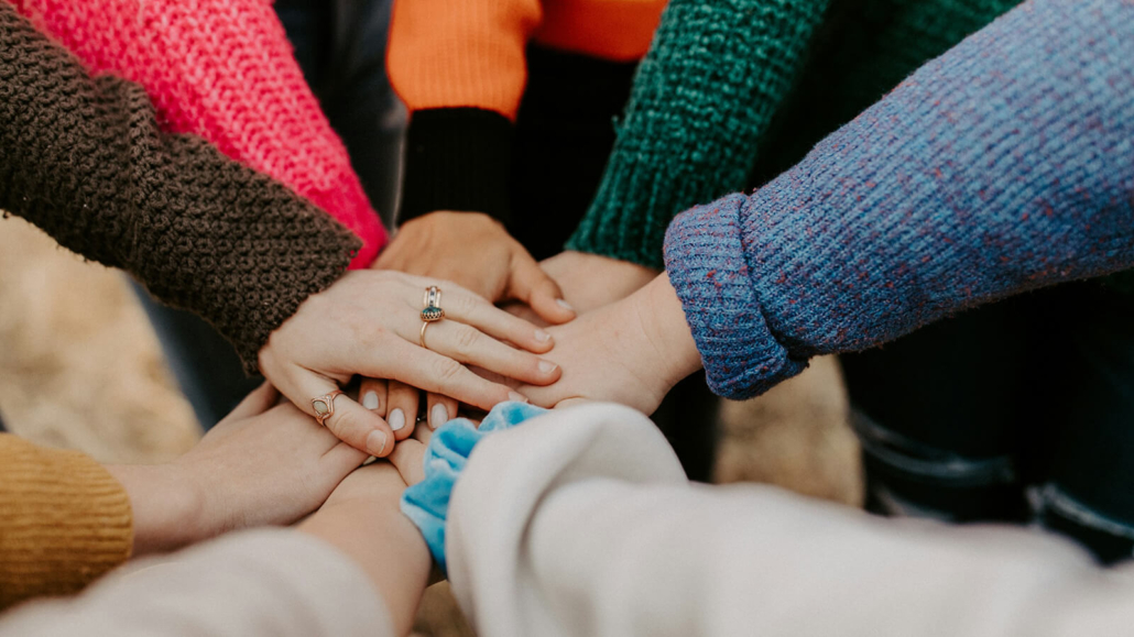Acht Menschen in Winterkleidung legen die Hände übereinander
