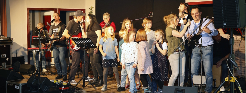 Kinder und die Band in Aktion auf der Bühne im Pfarrsaal von Schönbrunn-Vorpark