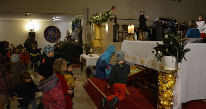 Kinder legen Strohhalme in die Krippe am Altar in Neufünfhaus