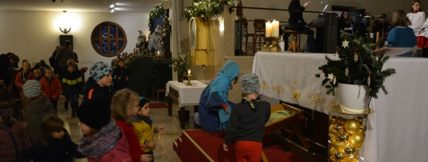 Kinder legen Strohhalme in die Krippe am Altar in Neufünfhaus
