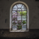 Ein altes zerbrochenes Rundbogenfenster mit Blick hinaus in einen verwilderten Garten