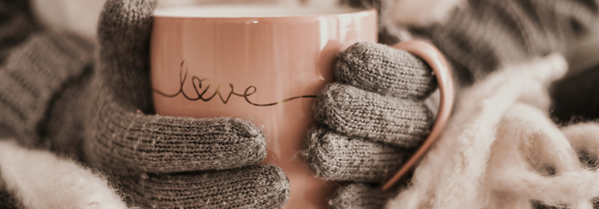 Zwei Hände in Handschuhen halten eine Teetasse auf der "Love" steht