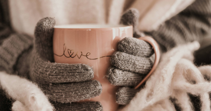 Zwei Hände in Handschuhen halten eine Teetasse auf der "Love" steht