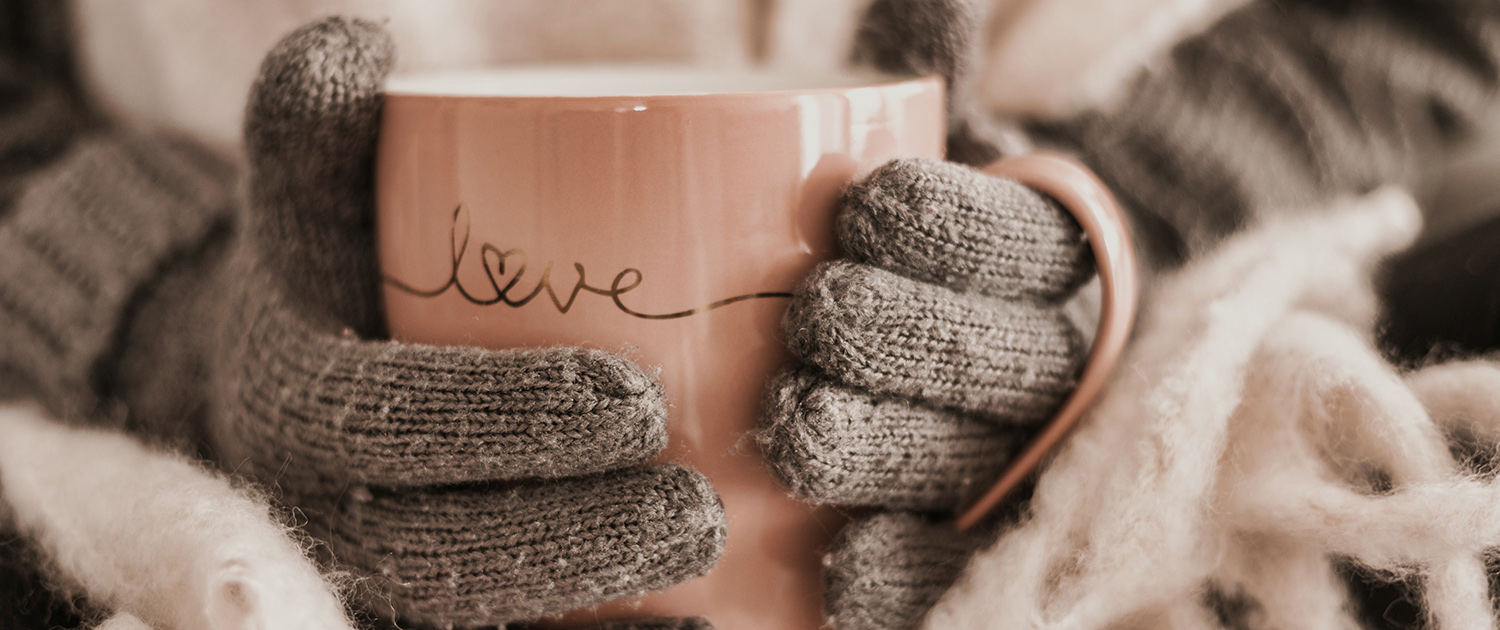 Zwei Hände in Handschuhen halten eine Teetasse auf der "Love" steht
