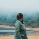 eine Frau dreht sich um und blickt auf einen See im Nebel