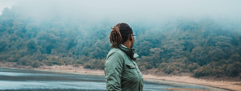 eine Frau dreht sich um und blickt auf einen See im Nebel