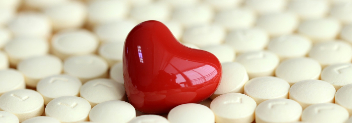 Ein rotes, glänzendes Herz zwischen weißen Tabletten